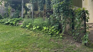 Een huis met schuin dak, een overdekte veranda en een tuin met gras en planten.