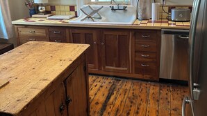 Een keuken met houten kastjes, een roestvrijstalen koelkast, een spoelbak met raam erboven en een houten aanrecht.