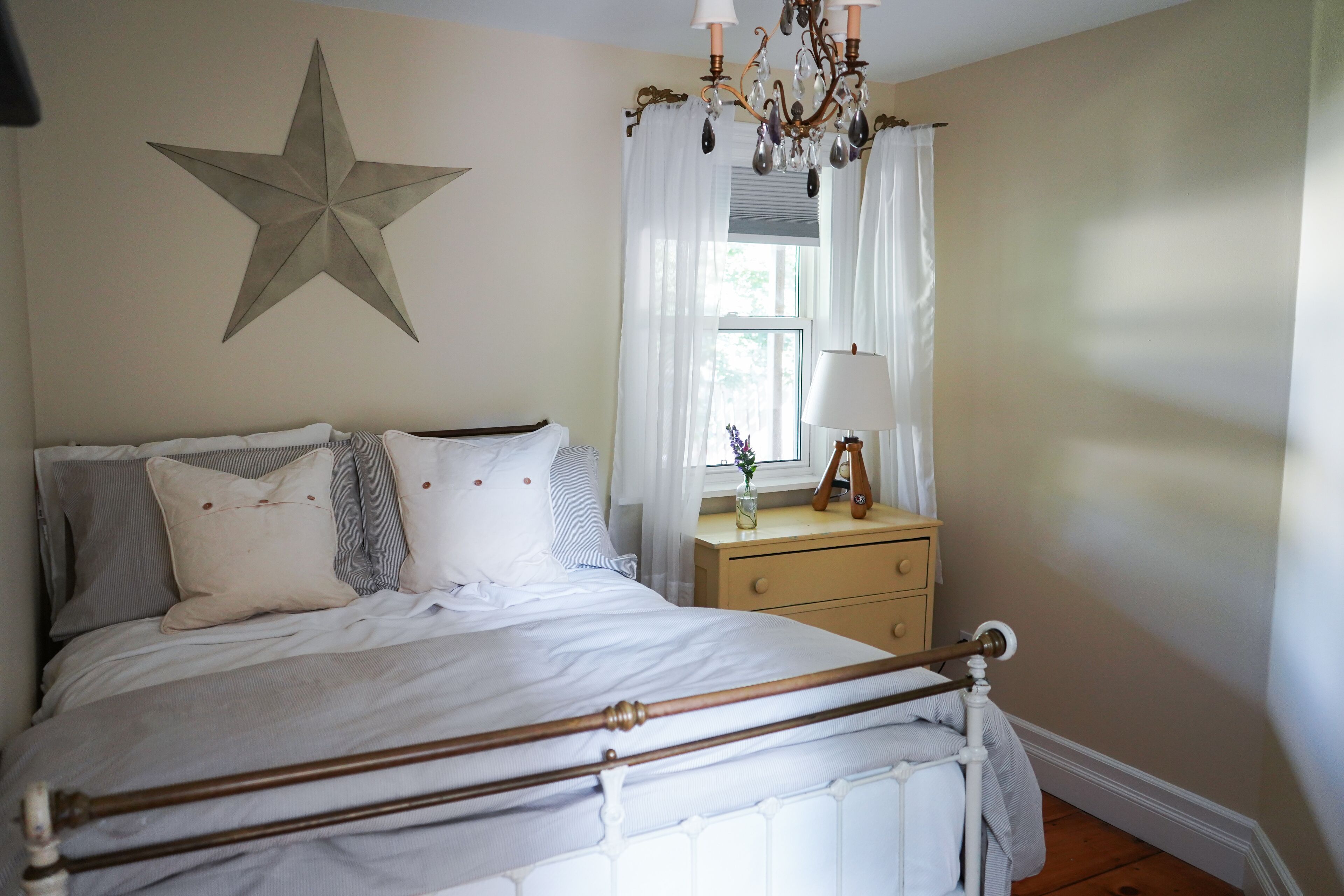 A bedroom with a bed, a nightstand, a dresser, a star decoration on the wall, and a window with curtains.