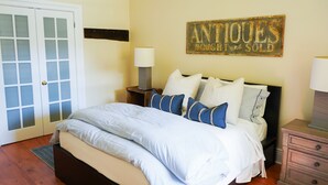 Een slaapkamer met een bed, nachtkastje, dressoir, lamp en een bord aan de muur.