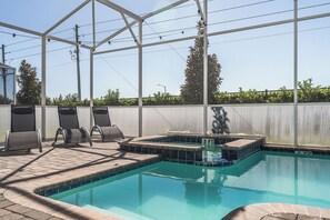 A swimming pool with a glass enclosure, lounge chairs, and a hot tub.