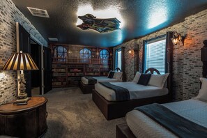 A bedroom with two beds, a large bookshelf, and a view of a snowy landscape through arched windows.