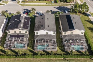 A residential area with three houses, each with a solar panel roof and a swimming pool.