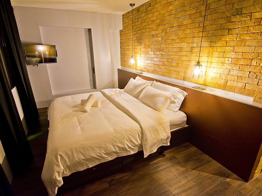 Una cama bien hecha en una habitación de hotel, con una pared de ladrillos y un televisor montado en la pared.