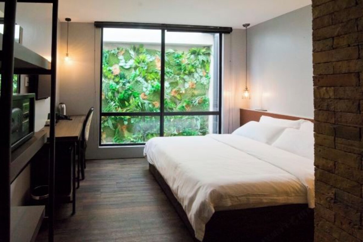 Une chambre avec une grande fenêtre, un lit, un bureau et un téléviseur.