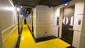 Pasillo de hotel con piso amarillo, un ascensor negro y un cartel que dice "01".