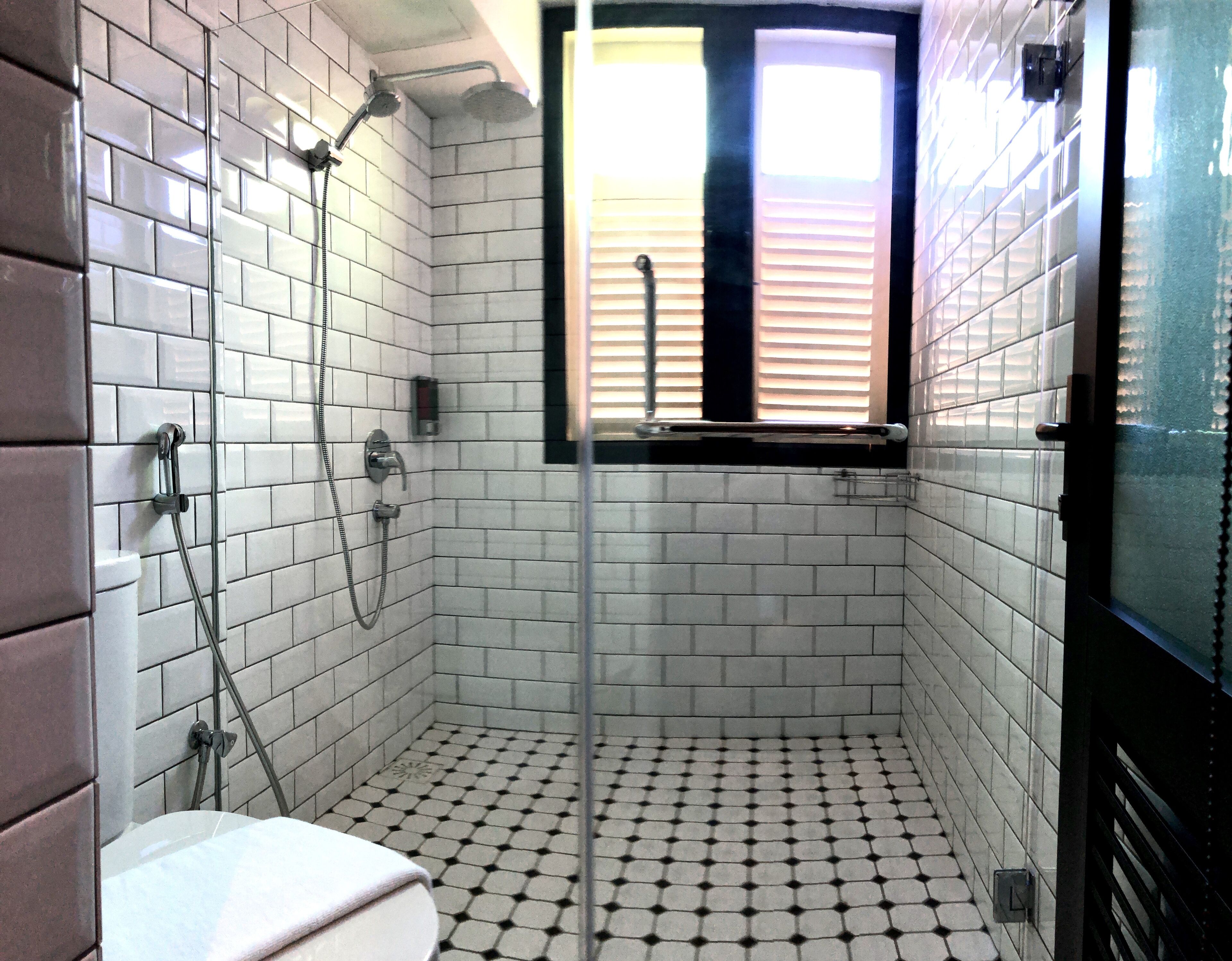 Un baño con azulejos blancos tipo metro, un inodoro, una ducha con puerta de vidrio y una ventana con persianas.