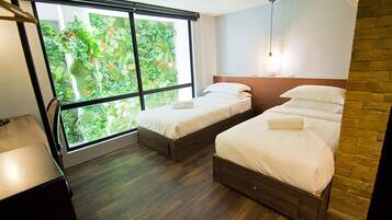 A hotel room with two beds, a large window with a view of greenery, and a brick accent wall.