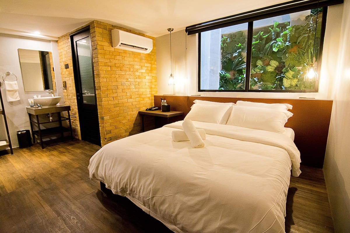 Hotelkamer met een groot bed, een badkamer met wastafel en spiegel, en een raam met uitzicht op groen.