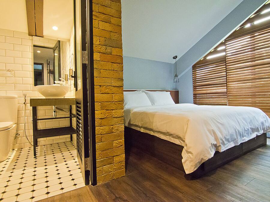 Un dormitorio con una cama, un baño con lavamanos y una pared de ladrillo.