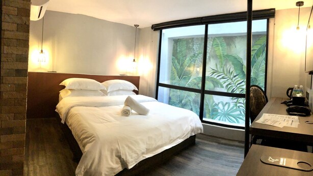 Hotelkamer met een groot bed, twee bedlampen, een bureau met stoel en een raam met uitzicht op een tropisch landschap.
