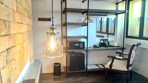 Een kamer met een bakstenen muur, een hanglamp, een houten stoel, een bureau met een computer en een raam met zonwering.