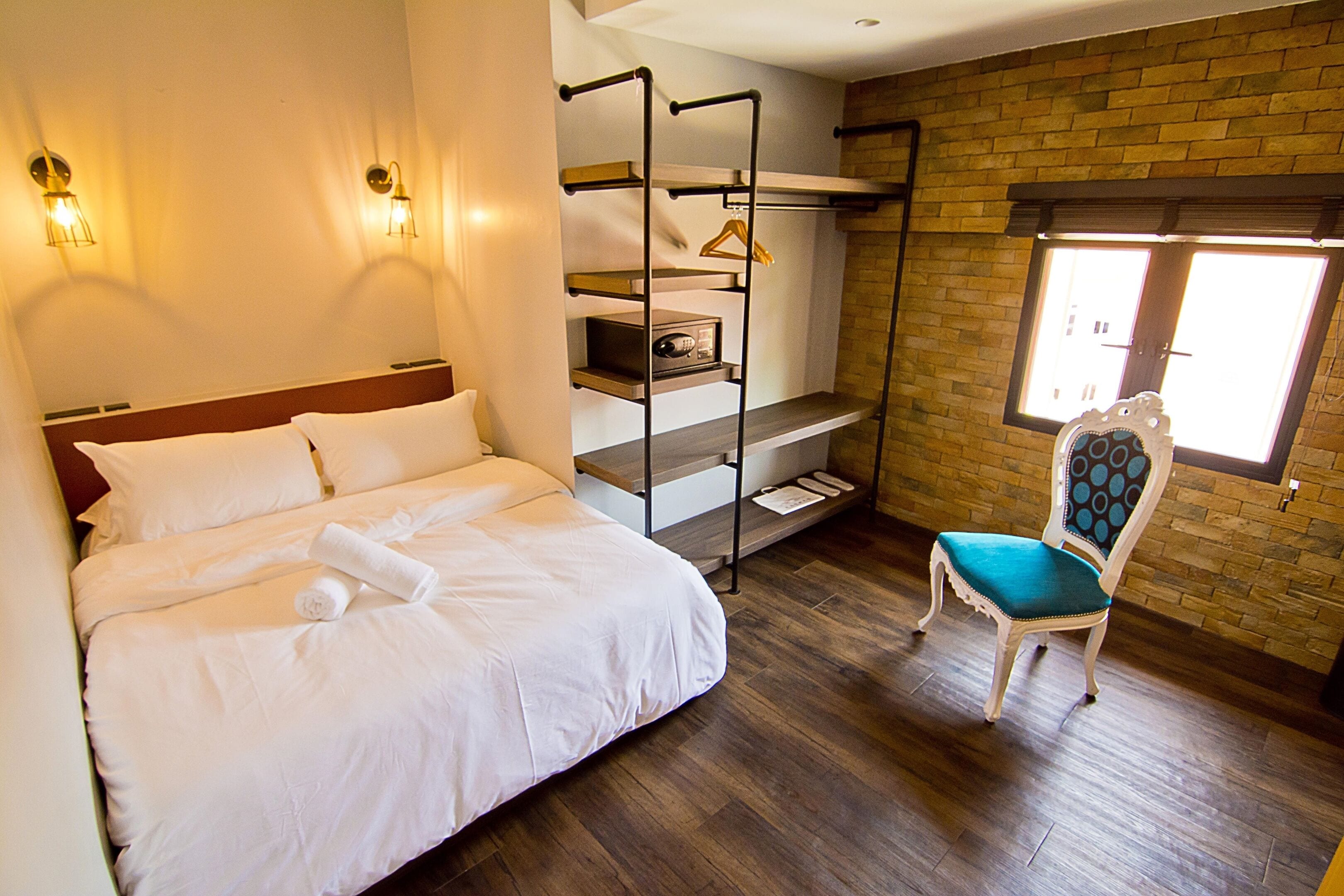 Een hotelkamer met een bed, een stoel, een stapelbed en een bakstenen muur.