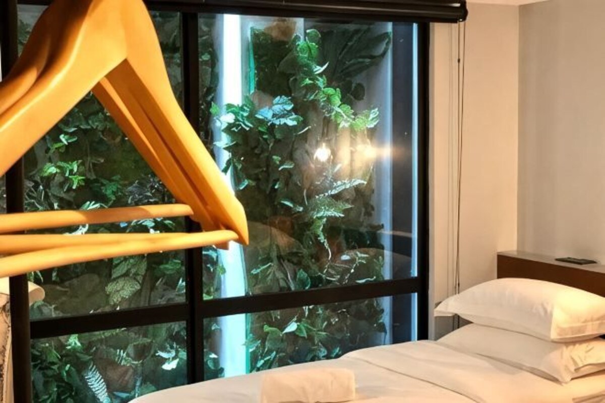 Un lit avec du linge de lit blanc, un cintre en bois et une fenêtre donnant sur un paysage verdoyant.