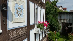 A traditional half-timbered building with a signboard, a window with flowers, and a bell. - VALUE HOF | cozy holiday house (Bracht)