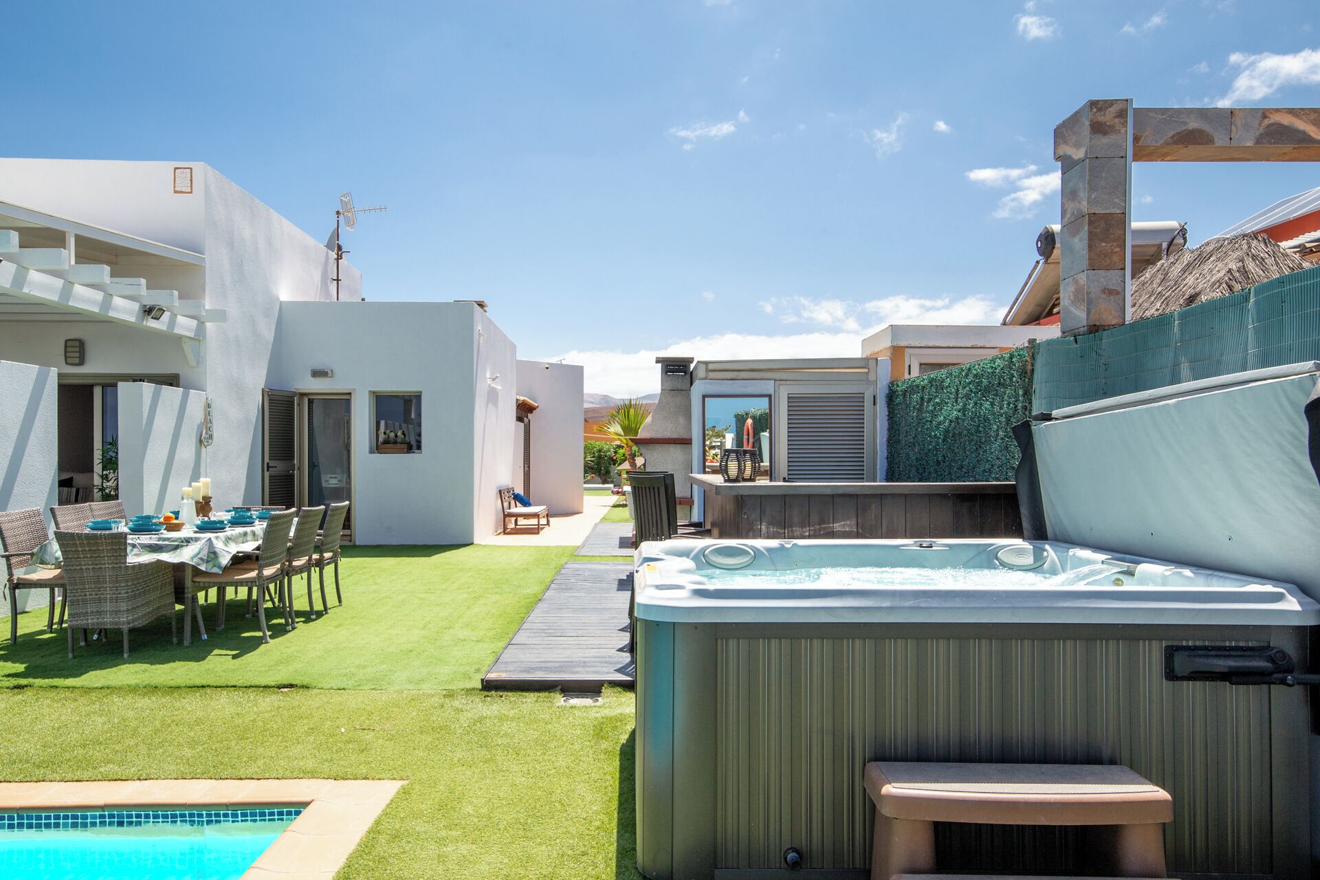 A modern outdoor patio with a hot tub, a dining area with wicker furniture, and a pool.