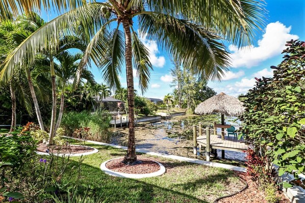 A tropical resort with palm trees, a thatched-roof hut, and a water body.