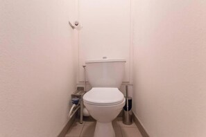 Ein kleines, schmales Badezimmer mit Toilette in Weiß, einem Metall-Bidet und einer kleinen Mülltonne.