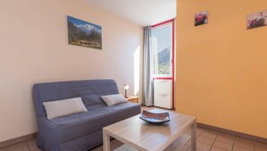 A room with a blue sofa, a wooden table, and a window with a view of mountains.