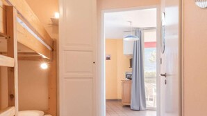 A room with a bunk bed, a wardrobe, and a door leading to a kitchen area.