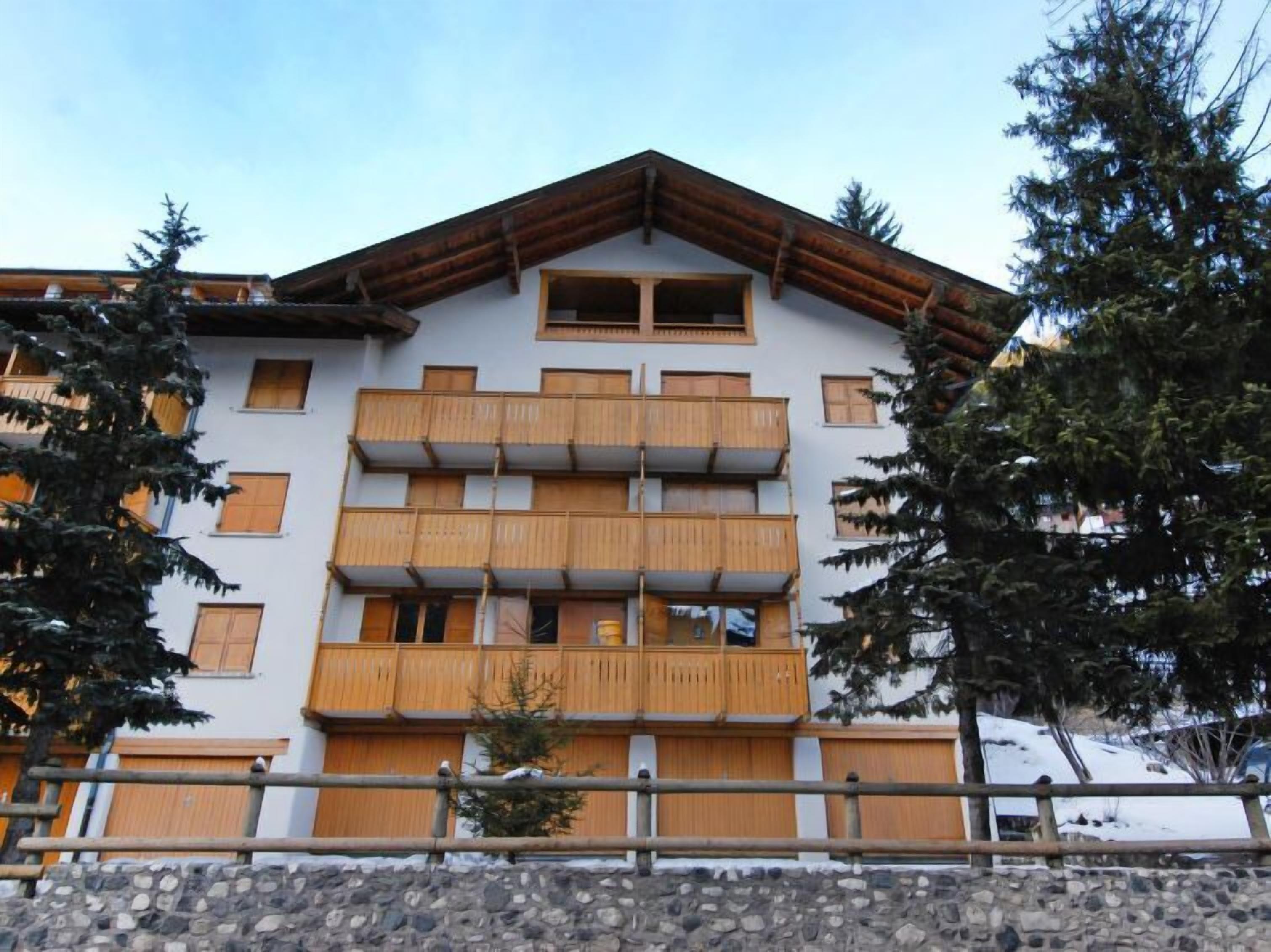 A multi-story building with wooden balconies, stone foundation, and surrounding trees.