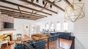 A spacious living area with a high ceiling, exposed beams, a brick fireplace, a dining area, and a kitchen with blue cabinets and pendant lighting. - 100ft to King St. Outdoor Space, Modern Design! (Charleston)