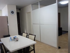 Une pièce avec une table et des chaises blanches, une horloge au mur et une porte coulissante.