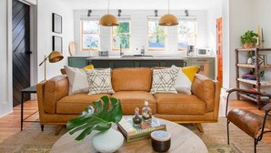 A modern living room with a brown leather sofa, a coffee table with decorative items, and pendant lights above. - Luxury Rental - Historic Charm - Central Location! (Charleston)