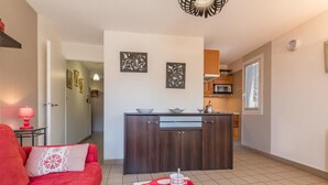 A compact living space with a kitchenette, a red sofa, a tray with cups, and artwork on the walls. - 150m from ski slopes, 4th floor, view mountain, balcony, tv, 31m², Serre Chevalier (Briançon)