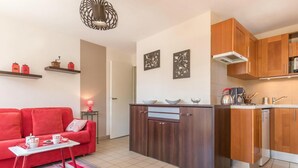 A compact living space with a kitchenette, a red sofa, and a small dining table. - 150m from ski slopes, 4th floor, view mountain, balcony, tv, 31m², Serre Chevalier (Briançon)