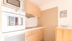 A compact kitchen with a built-in oven, microwave, and stovetop. It includes wooden cabinets and a small countertop. - 200m from resort center, 4th floor, balcony, tv, 30m², Serre Chevalier (Briançon)