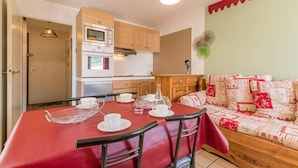 A compact kitchen with wooden cabinets, a built-in oven, and a dining area with a red tablecloth and chairs. - 200m from resort center, 4th floor, balcony, tv, 30m², Serre Chevalier (Briançon)