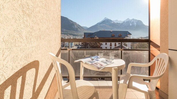 A balcony with a table and chairs, overlooking a mountain range and a town. - 200m from resort center, 4th floor, balcony, tv, 30m², Serre Chevalier (Briançon)