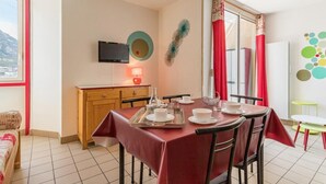 A dining area with a table set for four, a television mounted on the wall, and a window with red curtains. - 200m from resort center, 4th floor, balcony, tv, 30m², Serre Chevalier (Briançon)