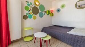 A compact room with a bed, a small table, two stools, and a wall with circular and floral decorations. - 200m from resort center, 4th floor, balcony, tv, 30m², Serre Chevalier (Briançon)