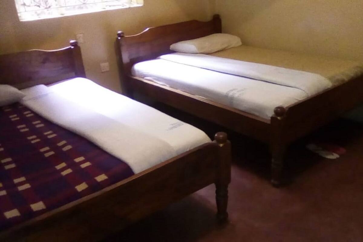 Two wooden beds with white bedding in a room with beige walls and a window.