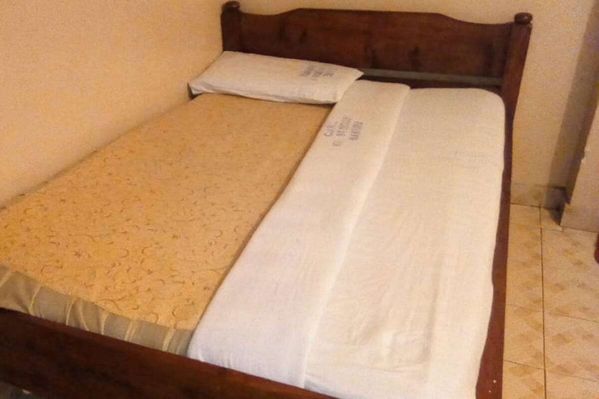 A single bed with a wooden frame, a beige patterned bedspread, and a white sheet.
