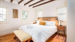 A bedroom with a wooden ceiling, a large bed with white bedding, a bedside table with a lamp, and a bench at the foot of the bed. - Gorgeous 6bd, 6ba Home, Made for Large Groups! (Charleston)