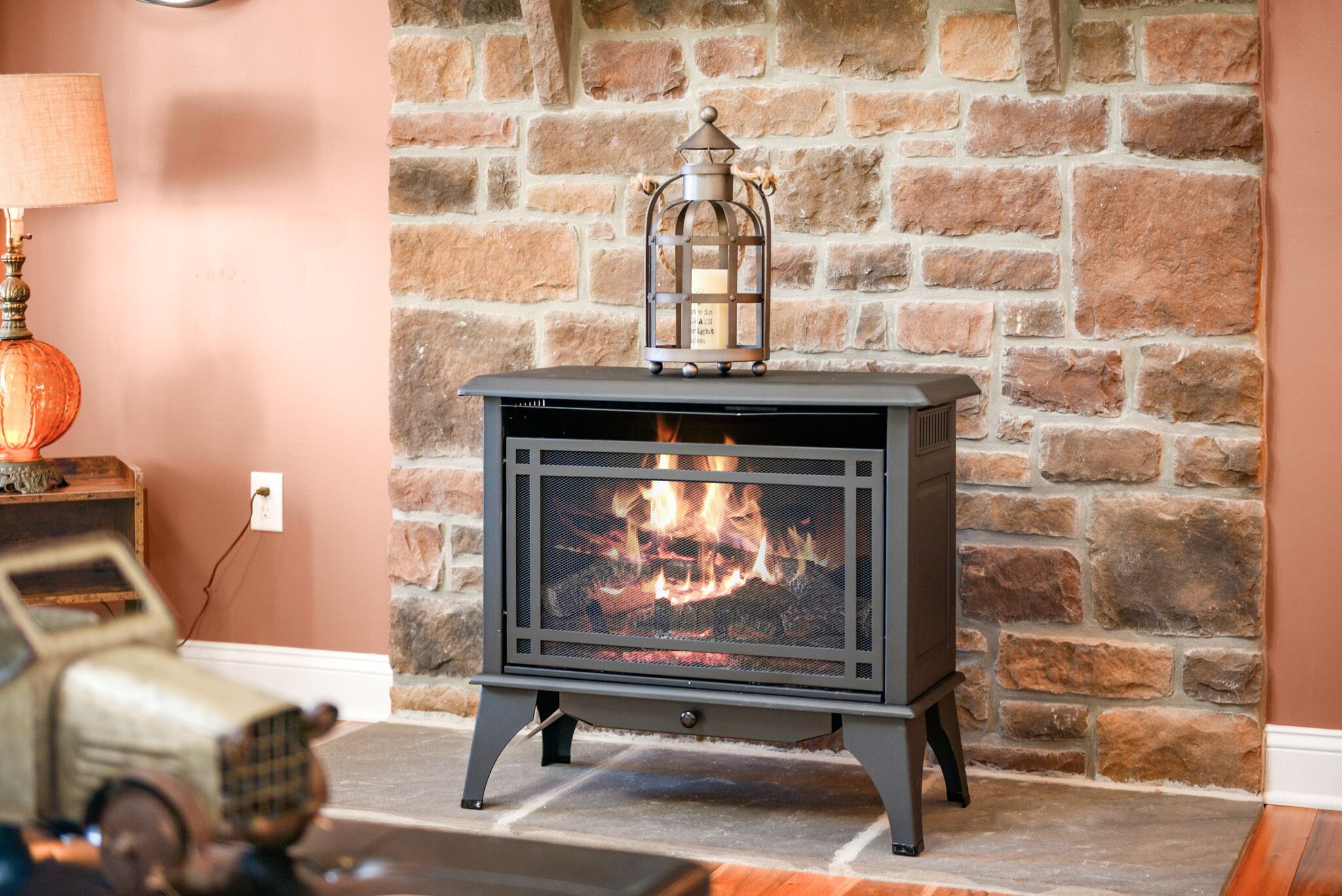 A wood-burning stove with a lantern on top, set against a stone wall.