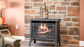 A wood-burning stove with a lantern on top, set against a stone wall.