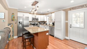 A modern kitchen with a central island, stainless steel appliances, and a 'Welcome' sign. - Charming "Cream of the Crop" Cape ~❤️of Middletown (Middletown)
