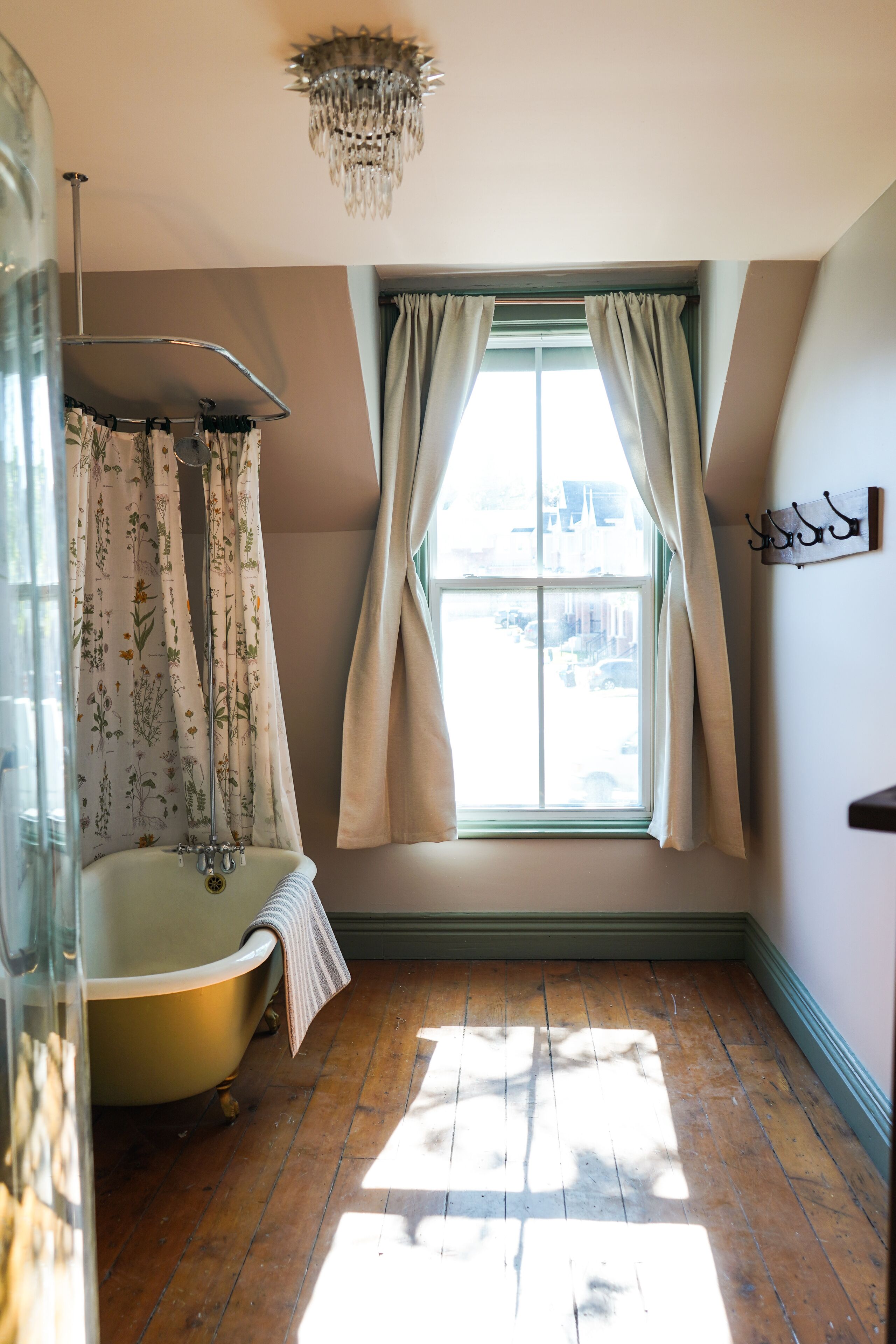 Een badkamer met een pootbad, een douchegordijn met bloemenprint en een raam met gordijnen.