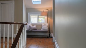 A staircase with a wooden handrail leading to a landing. There is a bench with cushions under a window, and a floor lamp is placed beside it. - Walk to Downtown or conservation area, 2 Bedroom home . Sleeps 4. Pets welcomed (Orangeville)