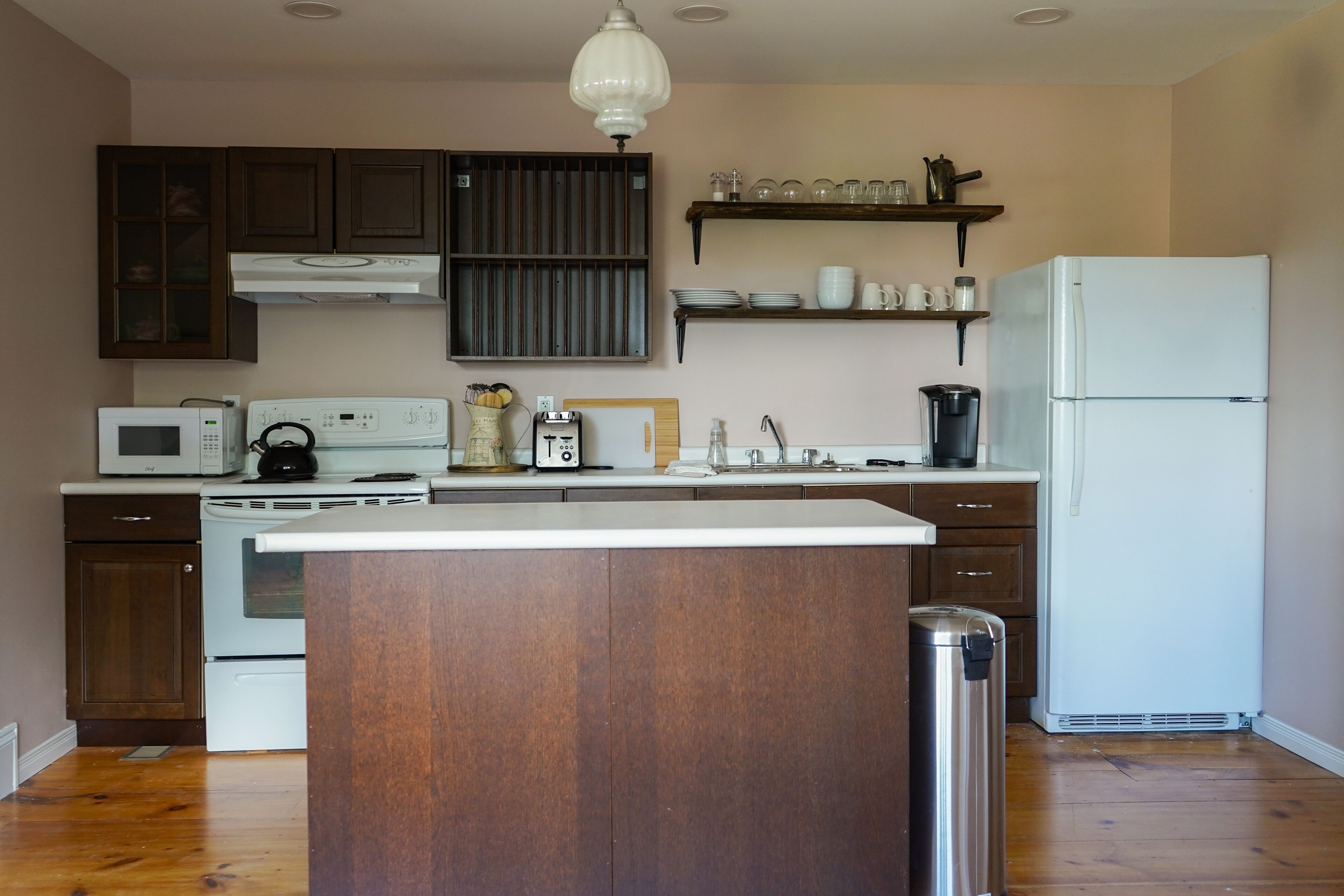 A kitchen with wooden cabinets, a white stove, a microwave, a refrigerator, and a hanging light fixture.