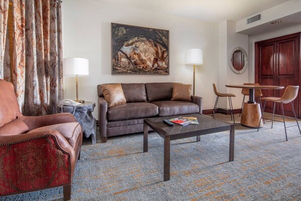 A living room with a brown leather sofa, a red armchair, a coffee table, and a painting of horses on the wall. - 406^ One Bedroom - Ski in/out + Ski Valet, 4 Season Pool & Spa! (Beaver Creek)