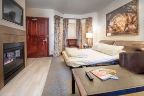 A hotel room with a bed, a sofa, a TV, a fireplace, and a painting. - 406^ One Bedroom - Ski in/out + Ski Valet, 4 Season Pool & Spa! (Beaver Creek)