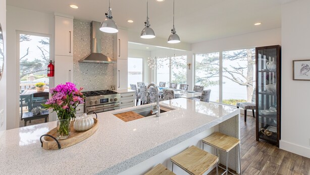 Une cuisine moderne dotée d’un grand îlot central, d’appareils électroménagers en acier inoxydable et de luminaires suspendus.