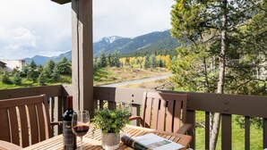 A wooden deck with a table, a bottle of wine, a glass, and a magazine.