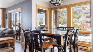 A dining area with a large table and chairs, large windows with a view of mountains, and a chandelier.