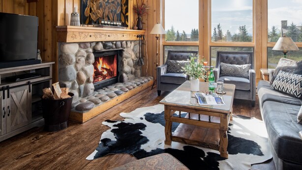 A cozy living room with a stone fireplace, wooden walls, a large window, and a leather sofa.